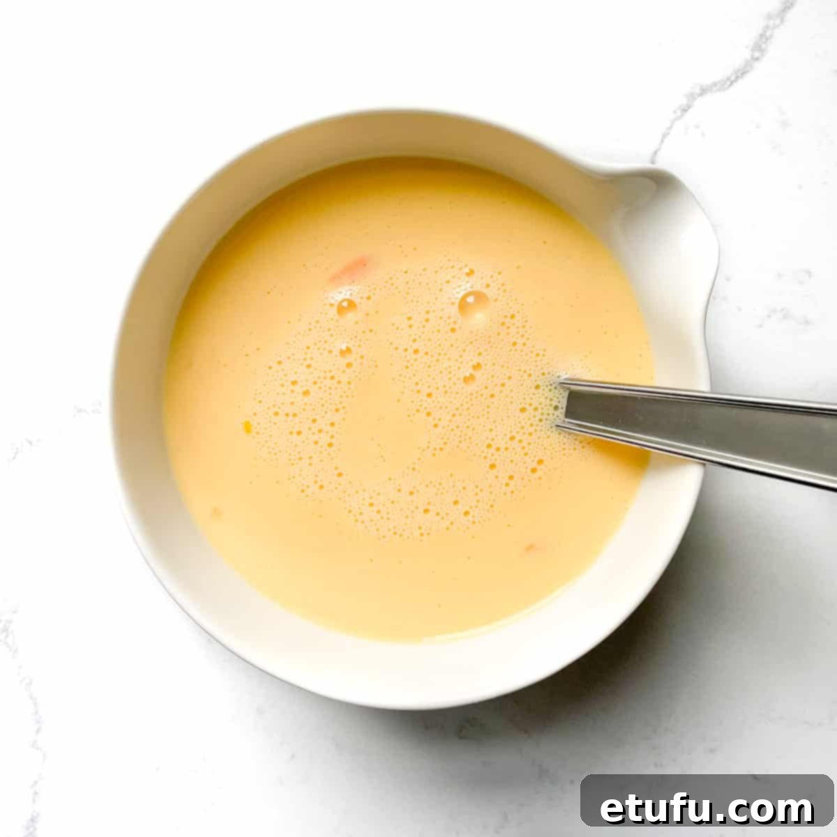 Eggs and milk whisked in a small white bowl.