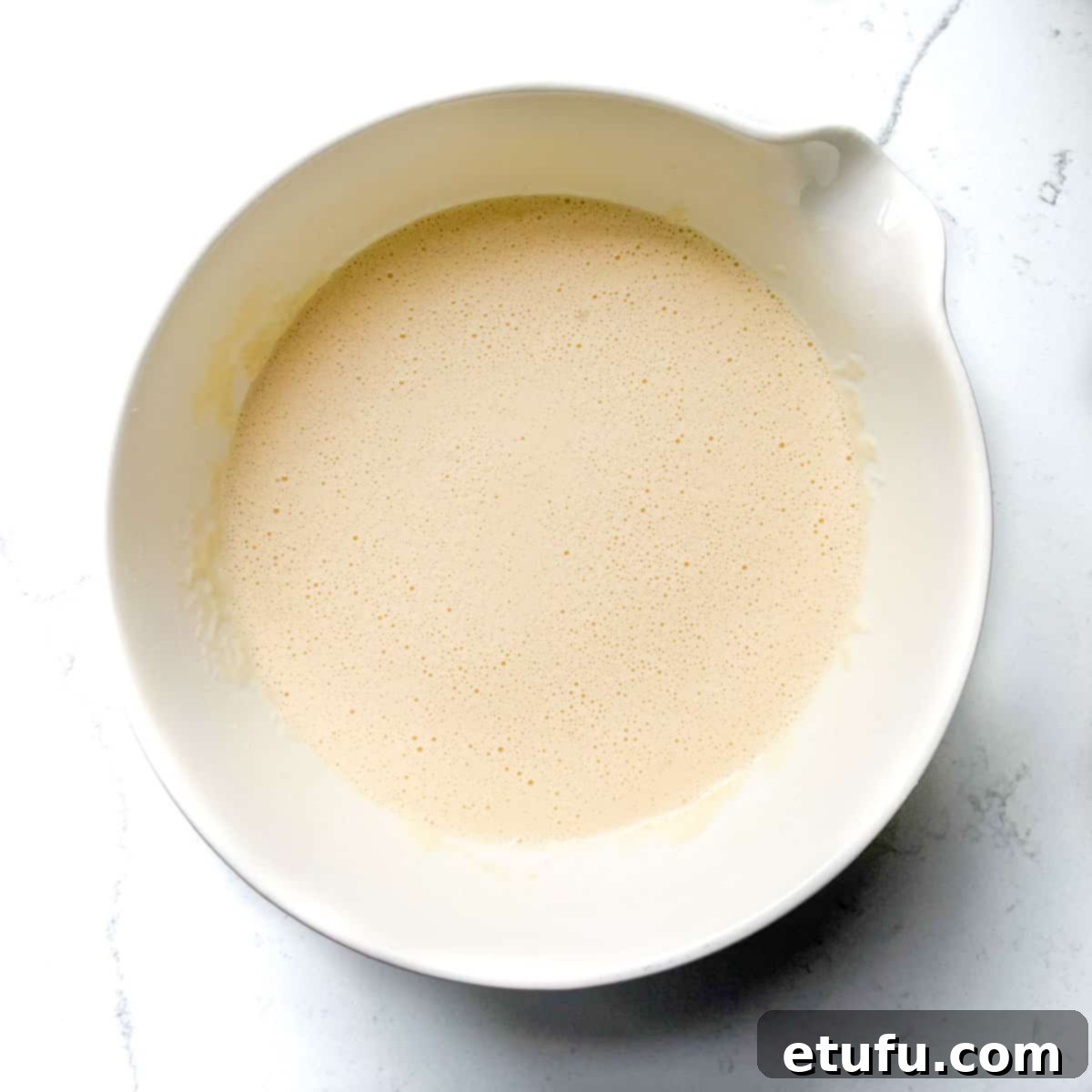 Mixed pandekager batter in a large white bowl, ready for frying.