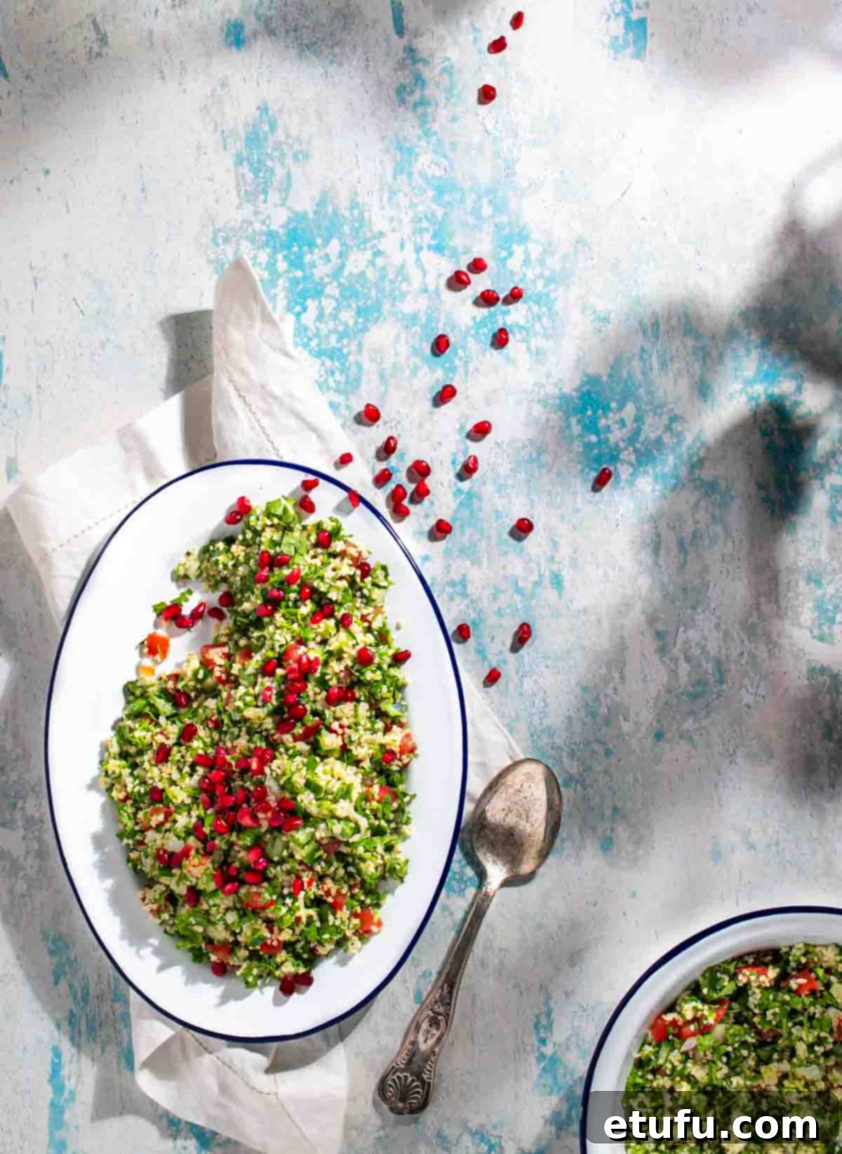 Taboule salad on a white oval plate, scattered with pomegranate seeds. 