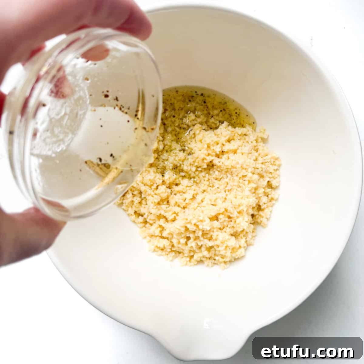 Adding the salad dressing to the bulgur wheat in a large white bowl.