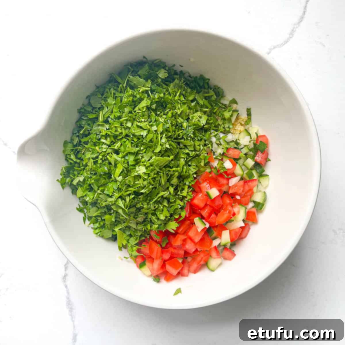 All the veg and herbs added to the bulgur in a large white bowl for the taboule.