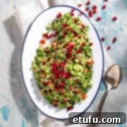 Taboule salad on a white oval plate, scattered with pomegranate seeds.