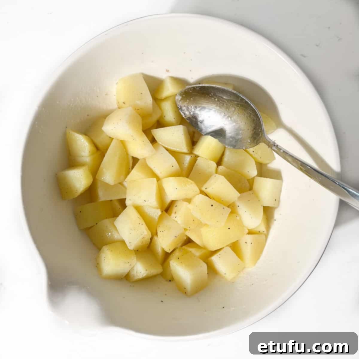 Potato cubes in a large white bowl with olive oil, salt and pepper stirred through.