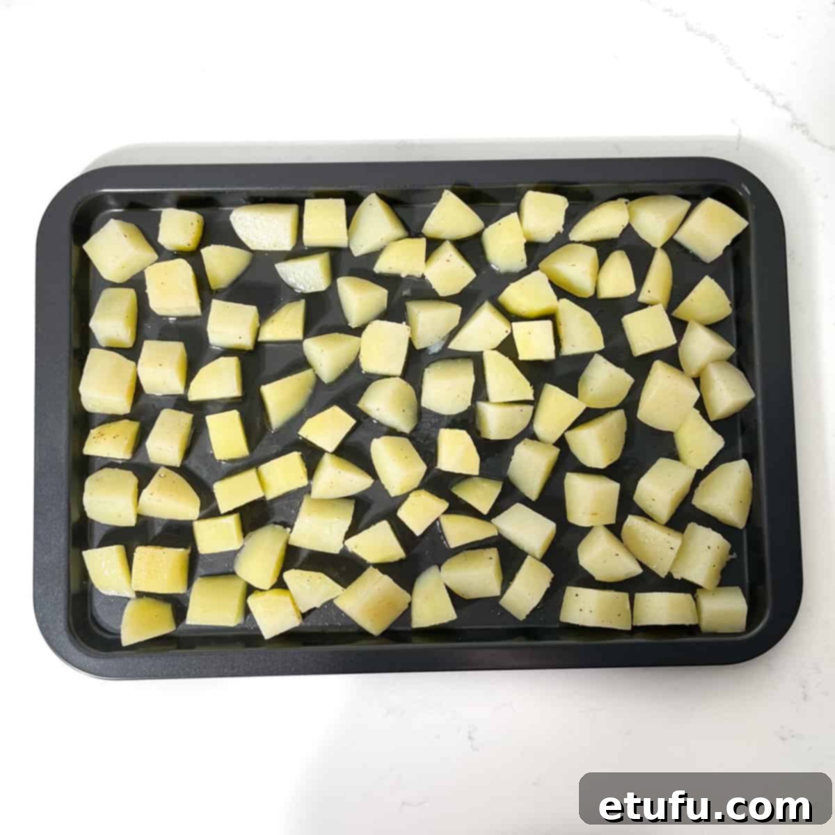 Parmentier potato cubes spread out on a baking tray in a single layer.