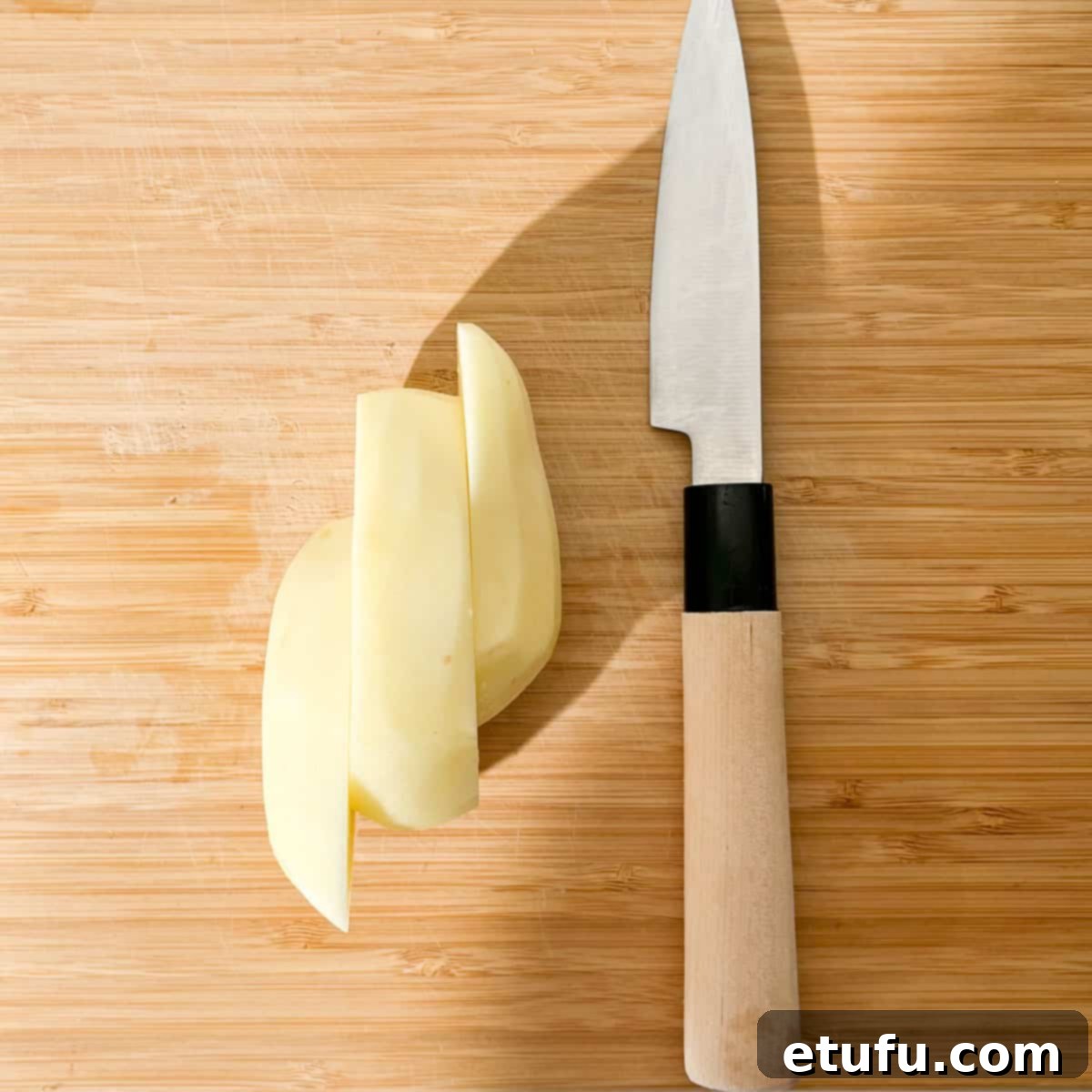 A potato on a cutting board, cut into thirds. 