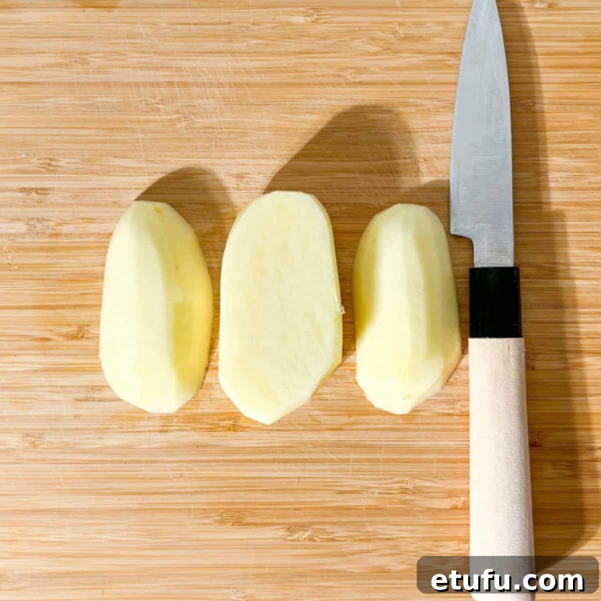 A potato on a cutting board, cut into thirds.