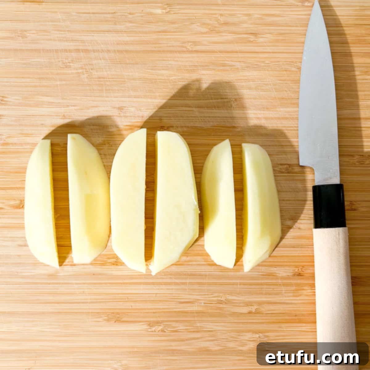 A potato on a cutting board, cut into six pieces.