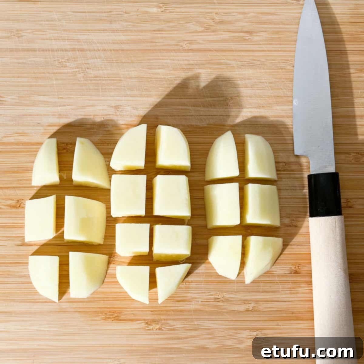 A potato on a cutting board cut into cubes.