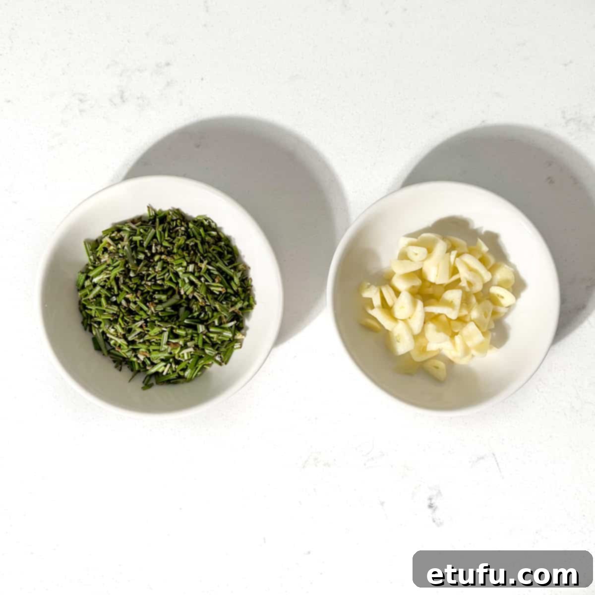 Chopped rosemary and garlic in two small white bowls.