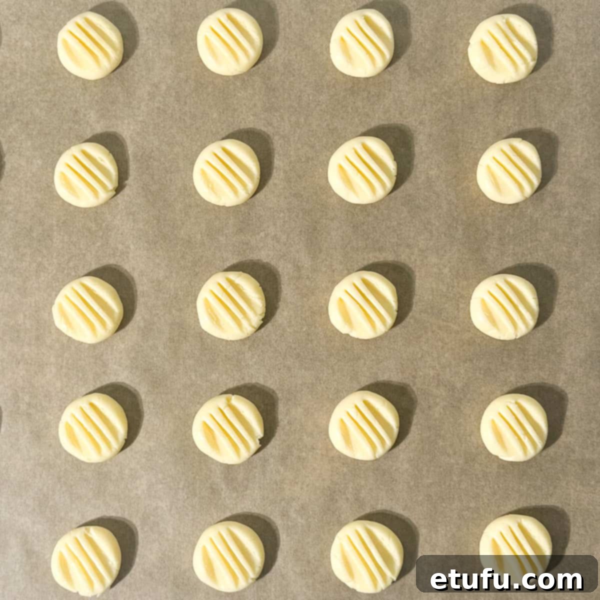 Unbaked sequilhos on a baking tray, flattened with a fork.