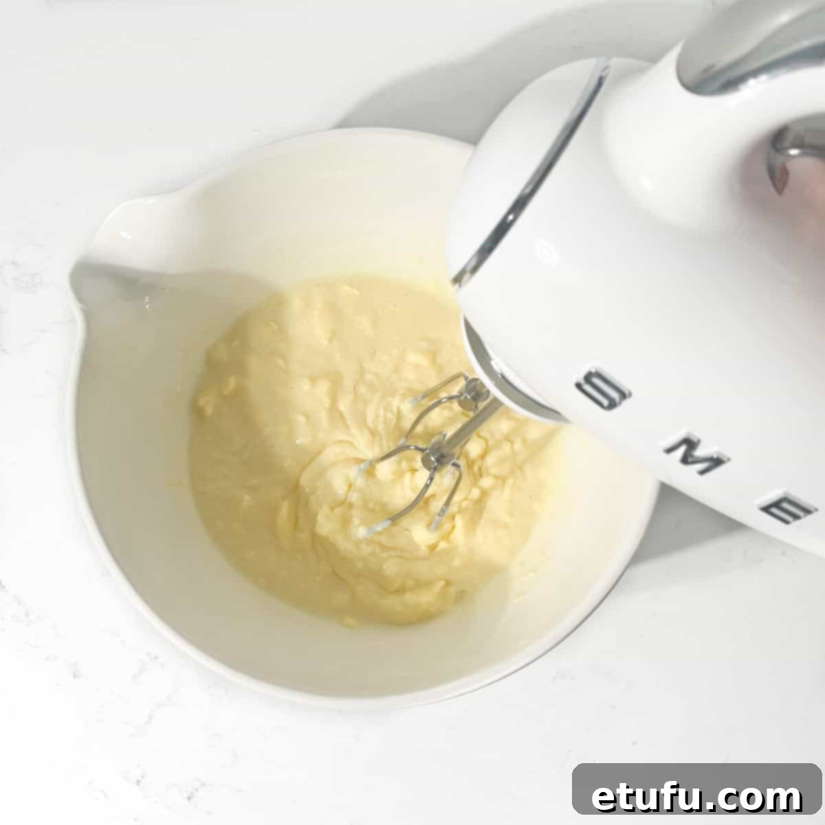 Mixing butter and condensed milk with an electric hand mixer in a large white bowl.