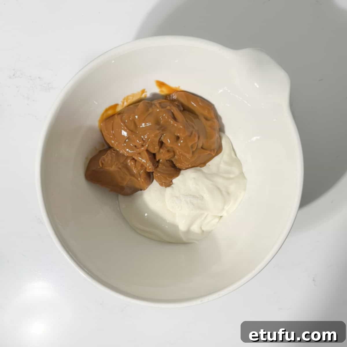 Adding dulce de leche and cream cheese to a large white mixing bowl.