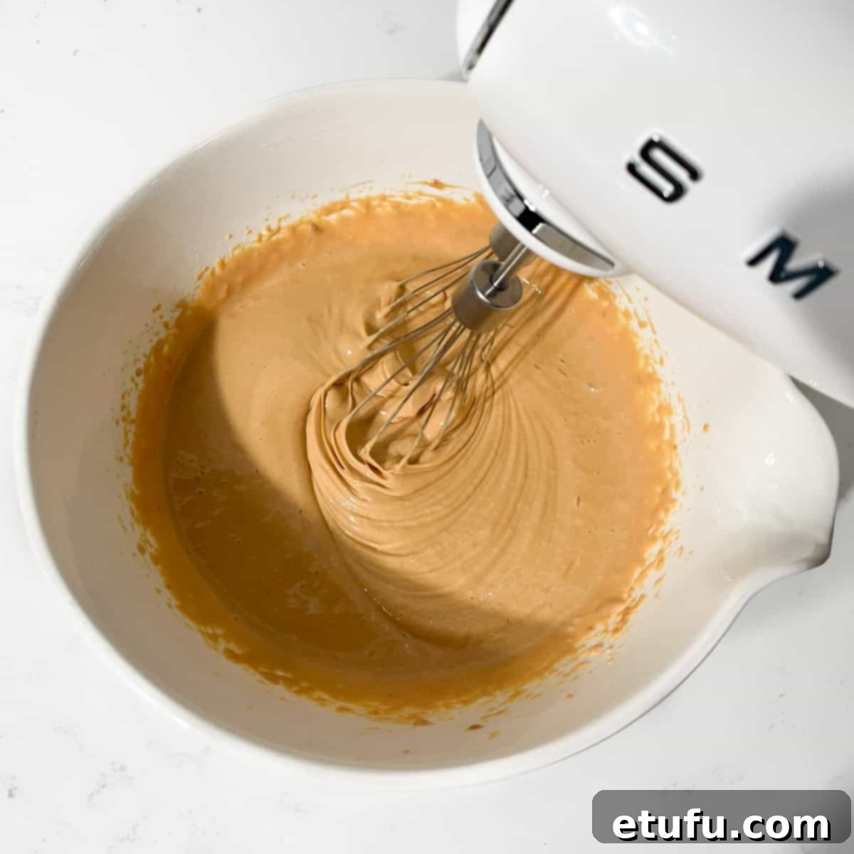 Beating together dulce de leche and cream cheese until smooth in a large white bowl.