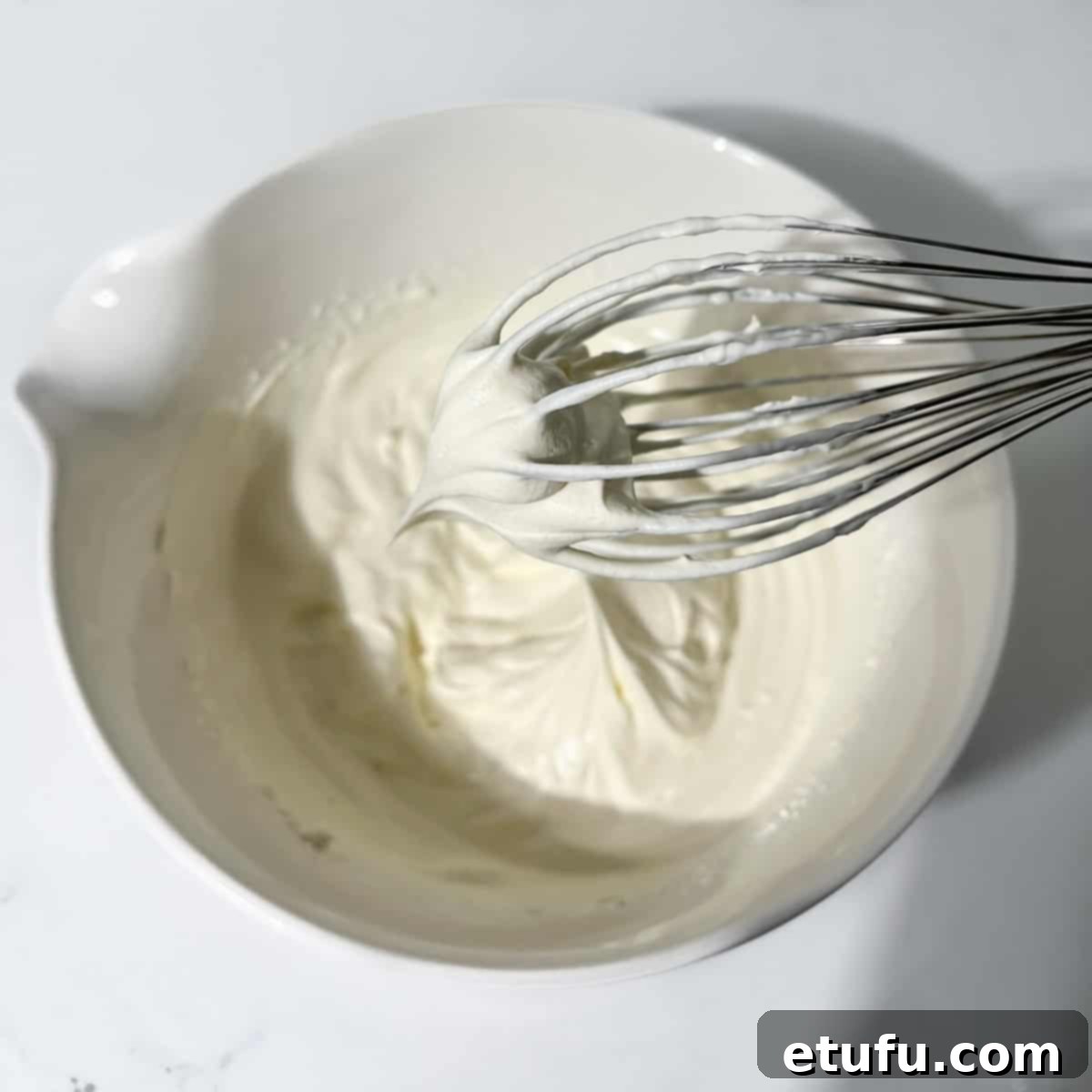 Whipping cold double cream in a separate large white bowl until soft peaks form.