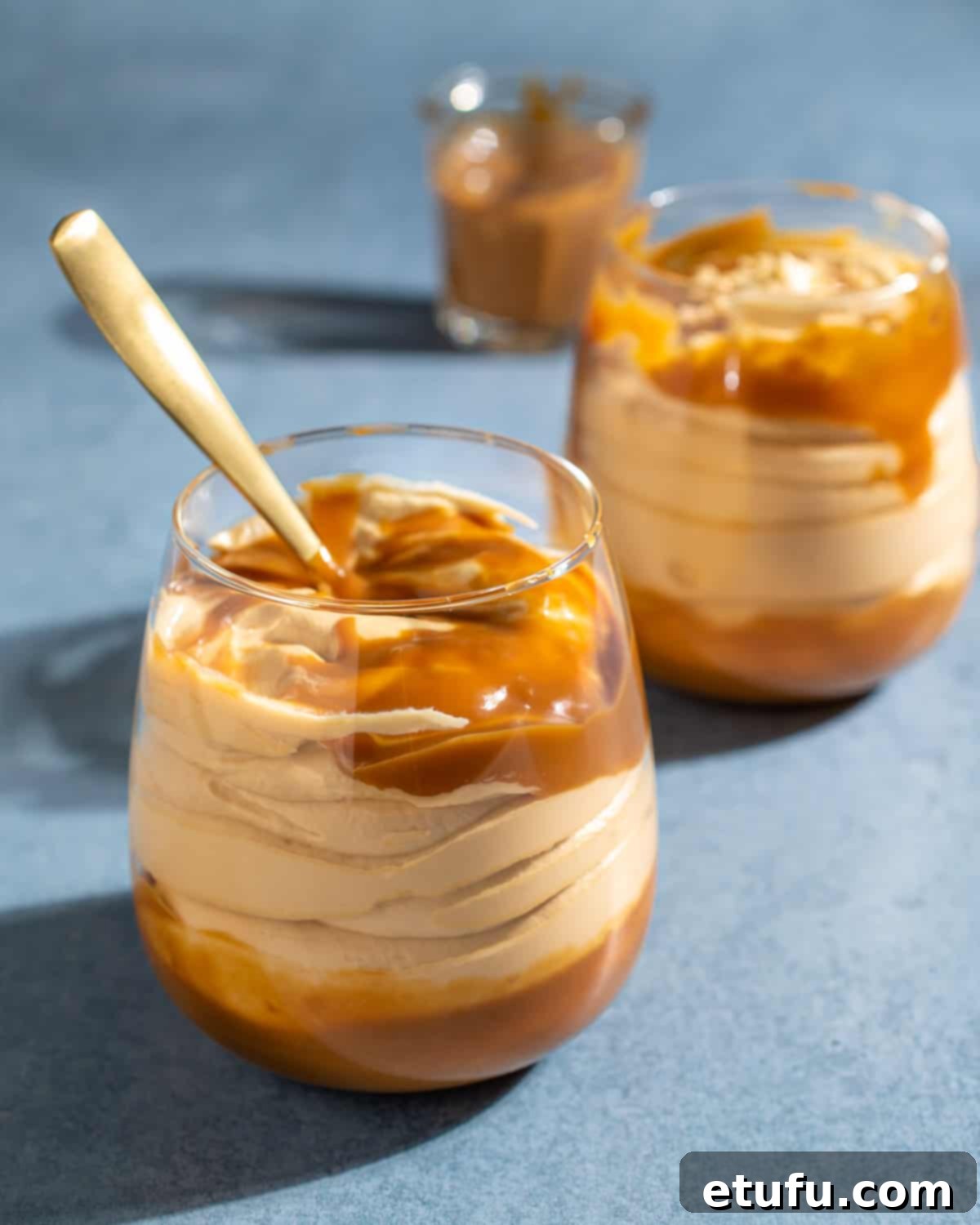 Dulce de leche mousse served in two glasses, expertly drizzled with additional dulce de leche sauce on top.