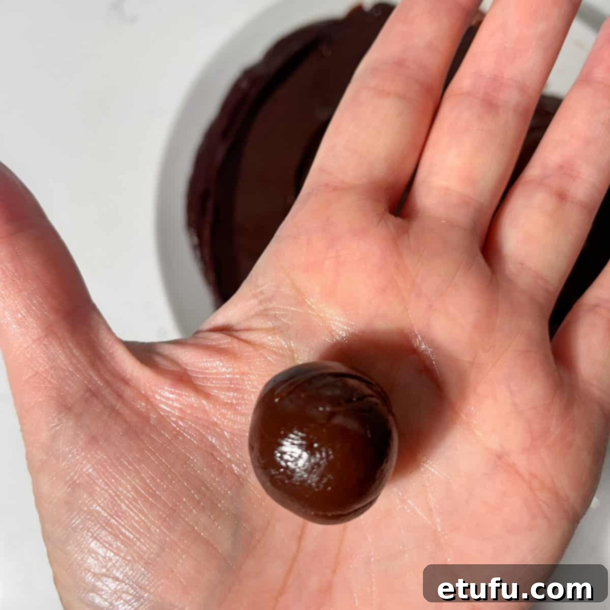 A hand holding one rolled ball of the mixture.