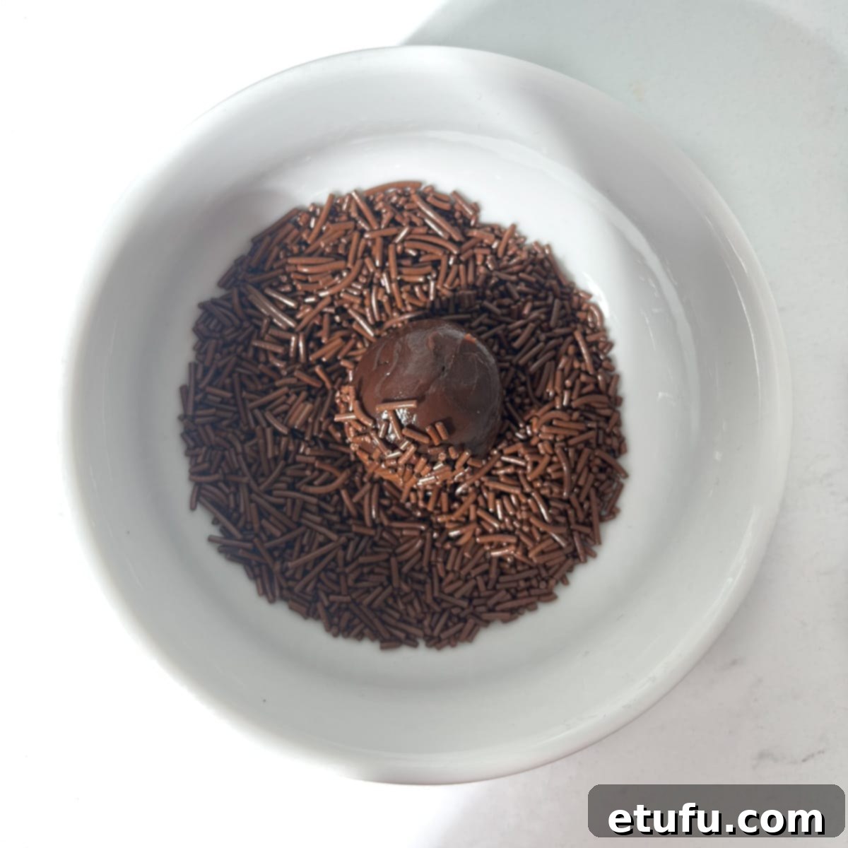 A brigadeiro ball in a small bowl of sprinkles.