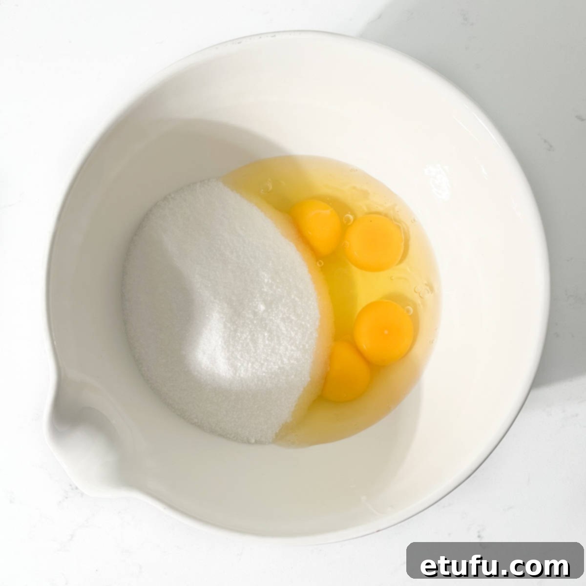 Sugar and eggs added to a large white bowl.