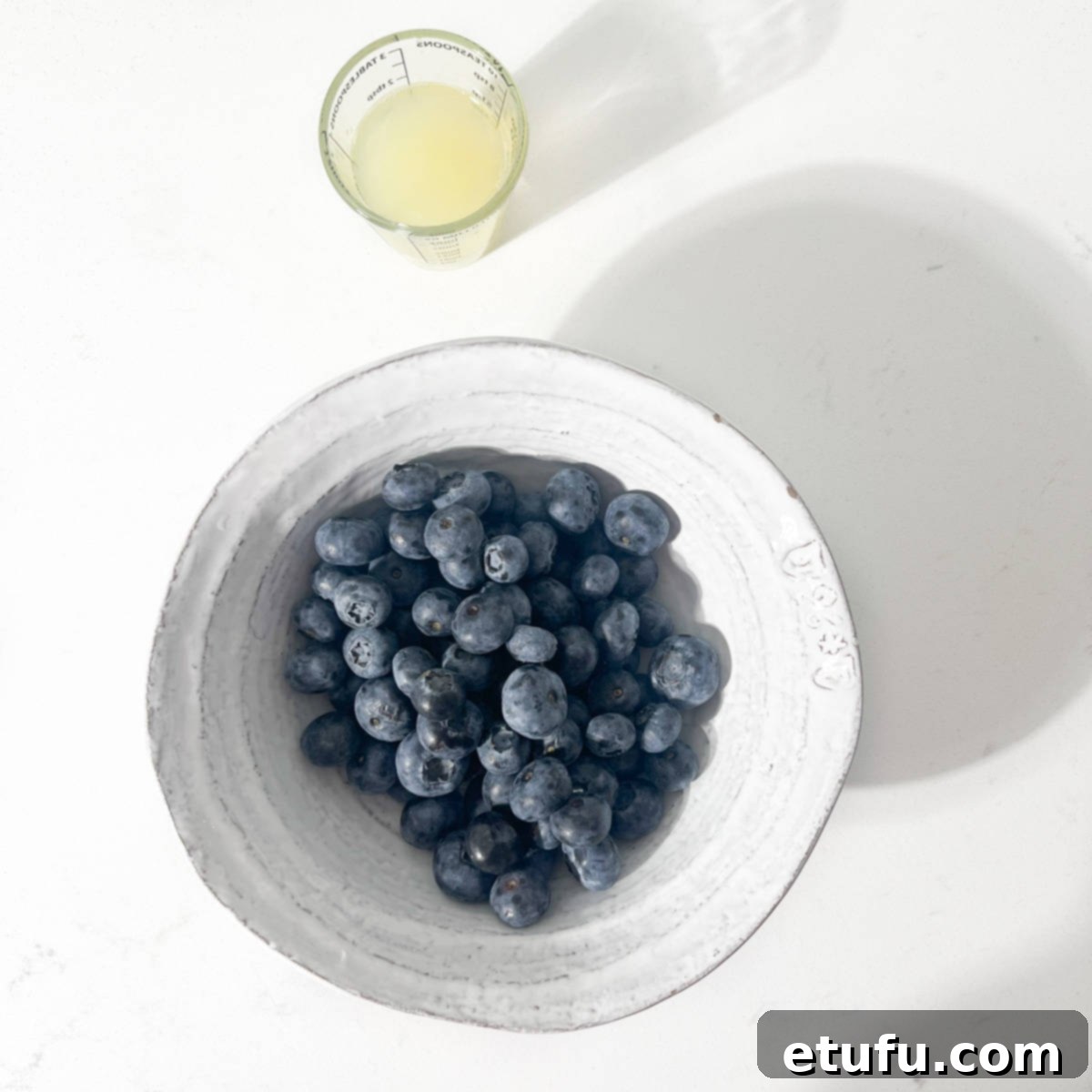 A bowl of blueberries and a small glass of lemon juice.