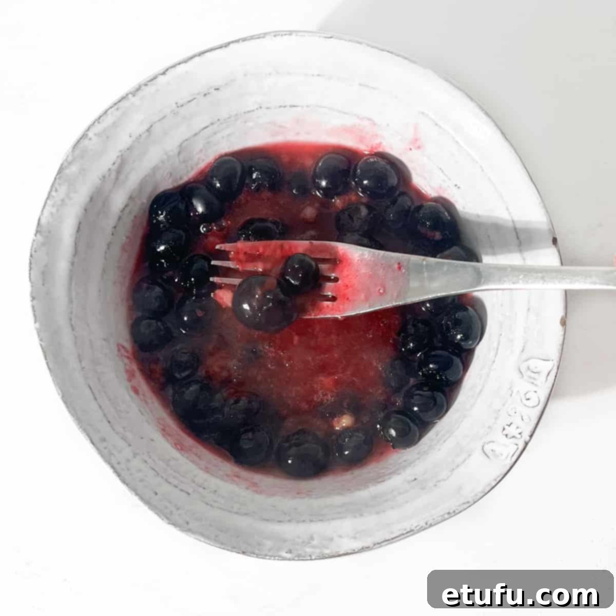 Blueberries in a bowl being squashed with a fork.