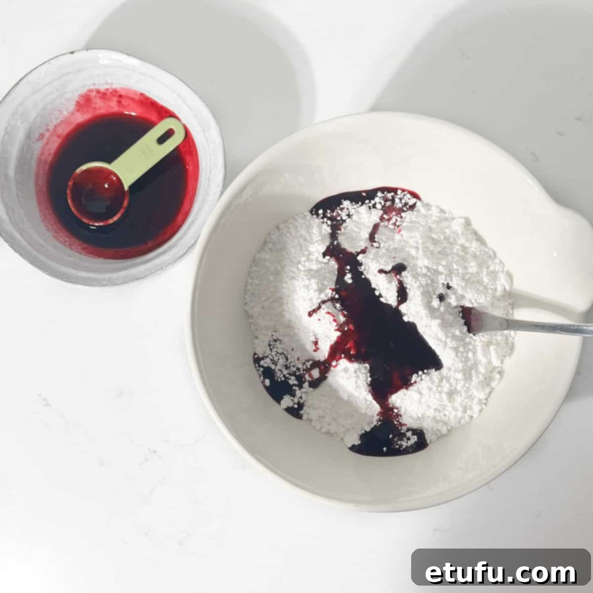 Adding a few tablespoons of blueberry juice to the icing sugar in a large white bowl.