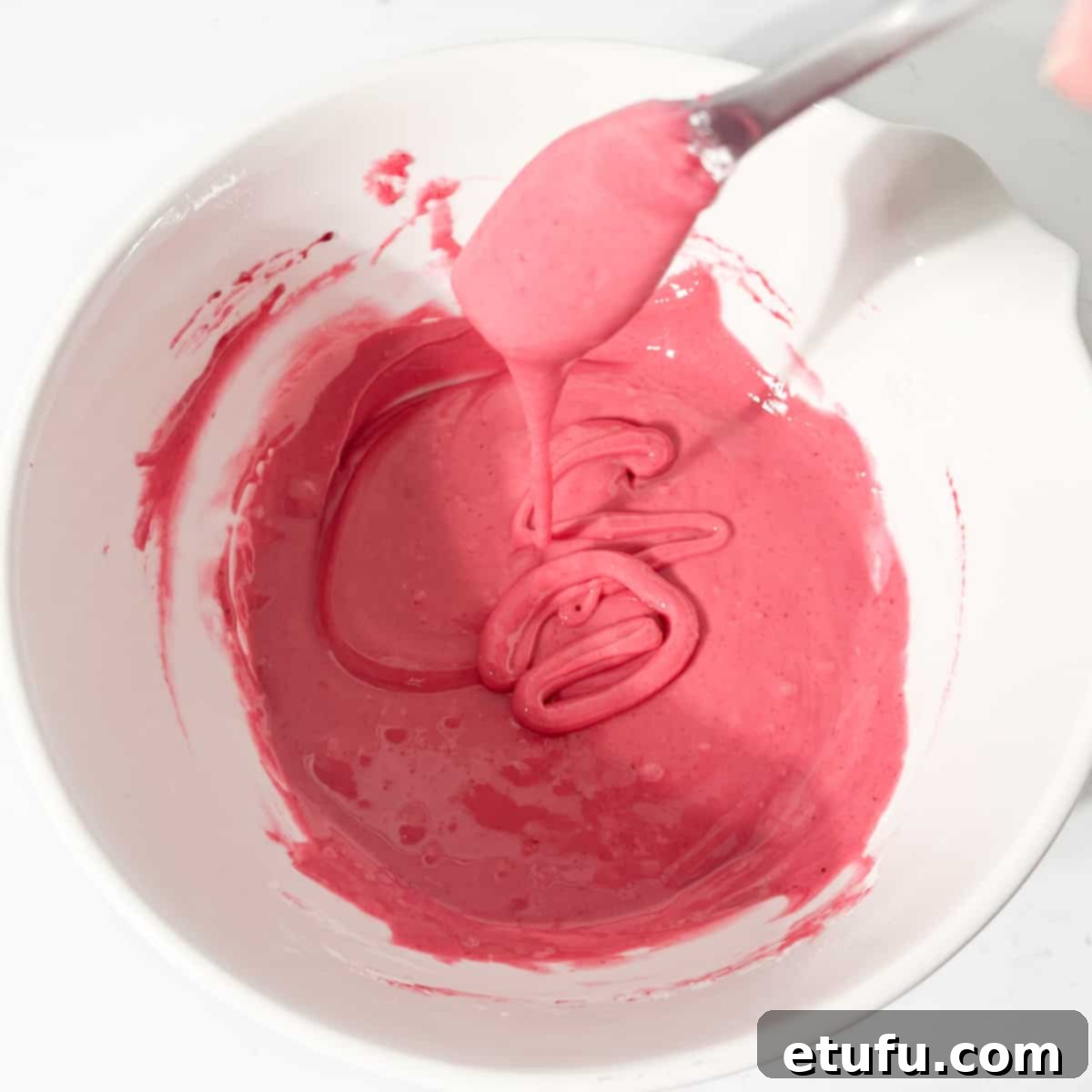 The pink icing for the Tottenham cake at a thick but fluid consistency in a large, white bowl.