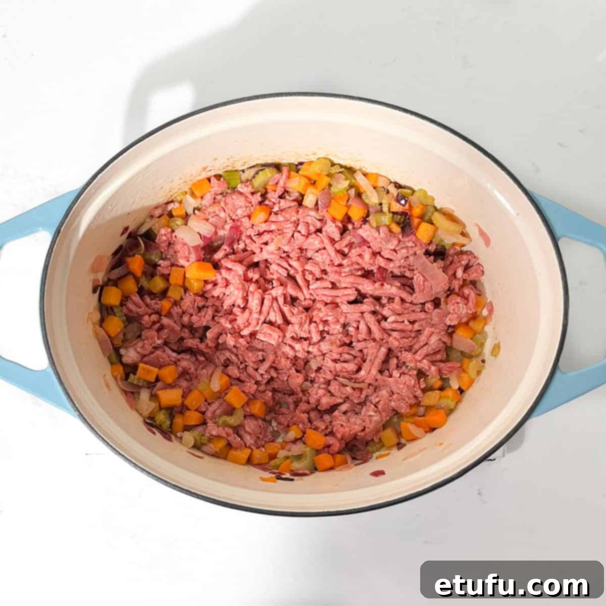 Adding raw mince to the large pot with cooked vegetables.