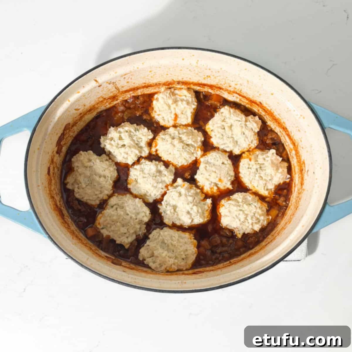 Raw dumpling balls added to the cooked mince in a large pot.