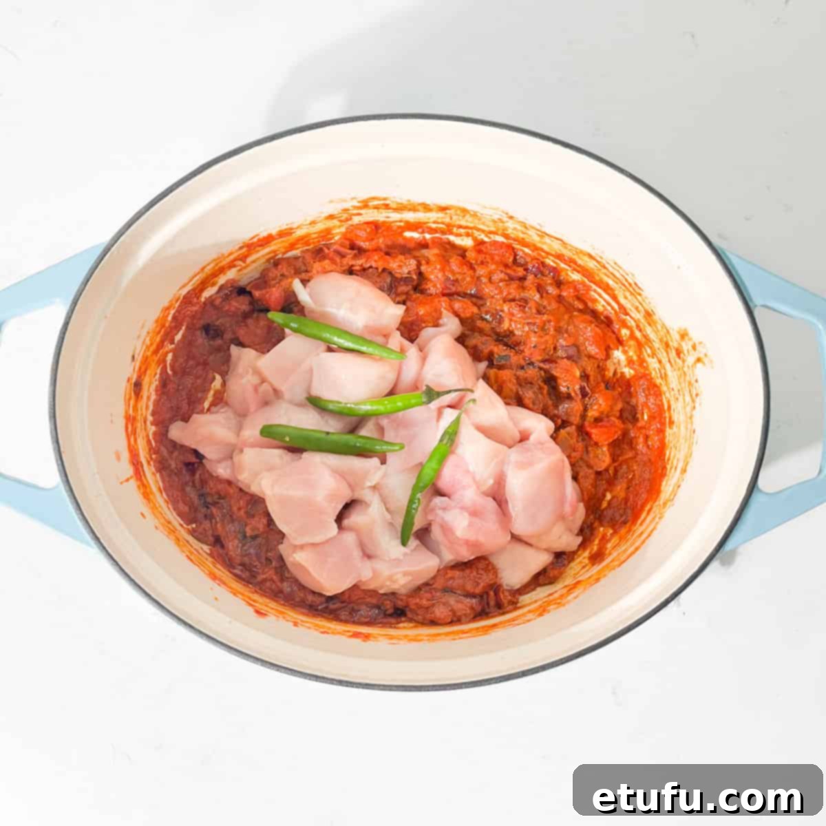 Adding the raw chicken and green chillies to the tomato based for the Chicken Handi in a large pot.