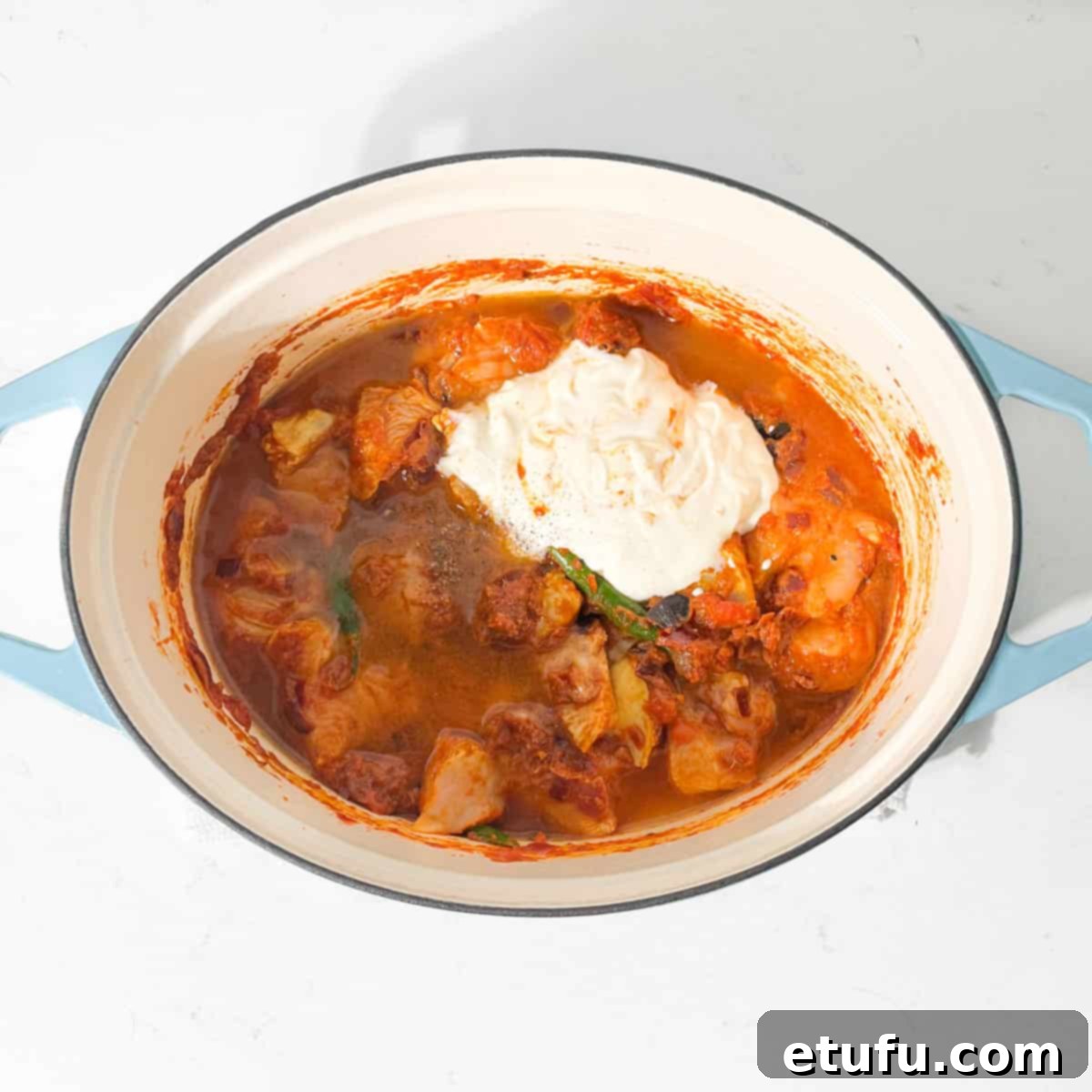Adding yoghurt to the chicken handi in a large oval pot.