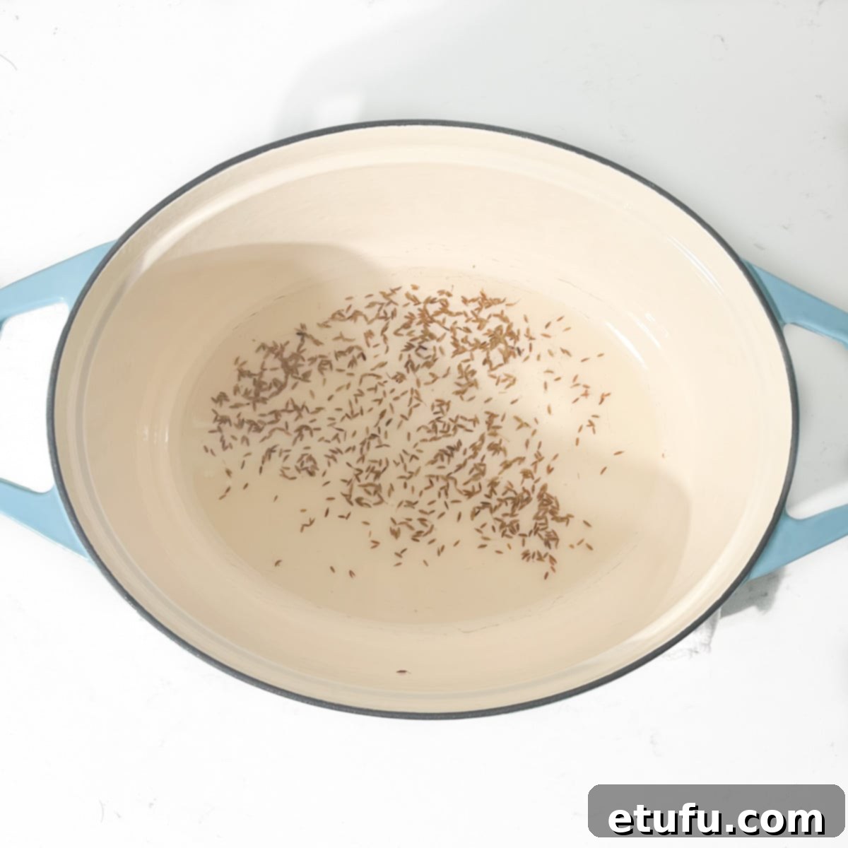 Frying cumin seeds in hot oil in a large oval pot.