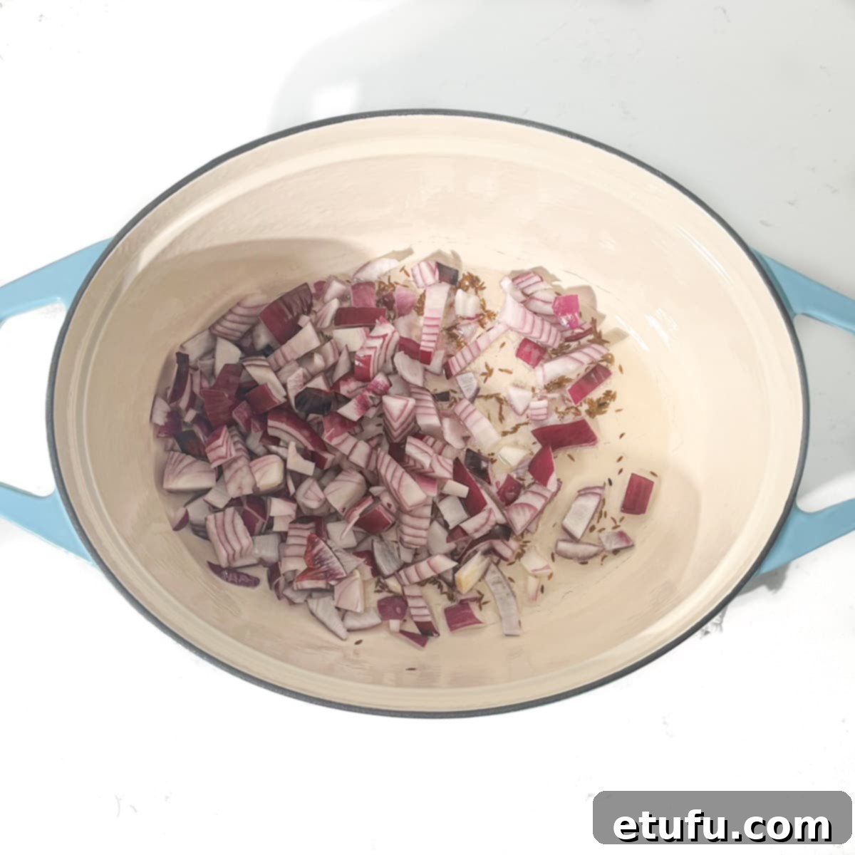 Adding onions to a large oval pot for frying.