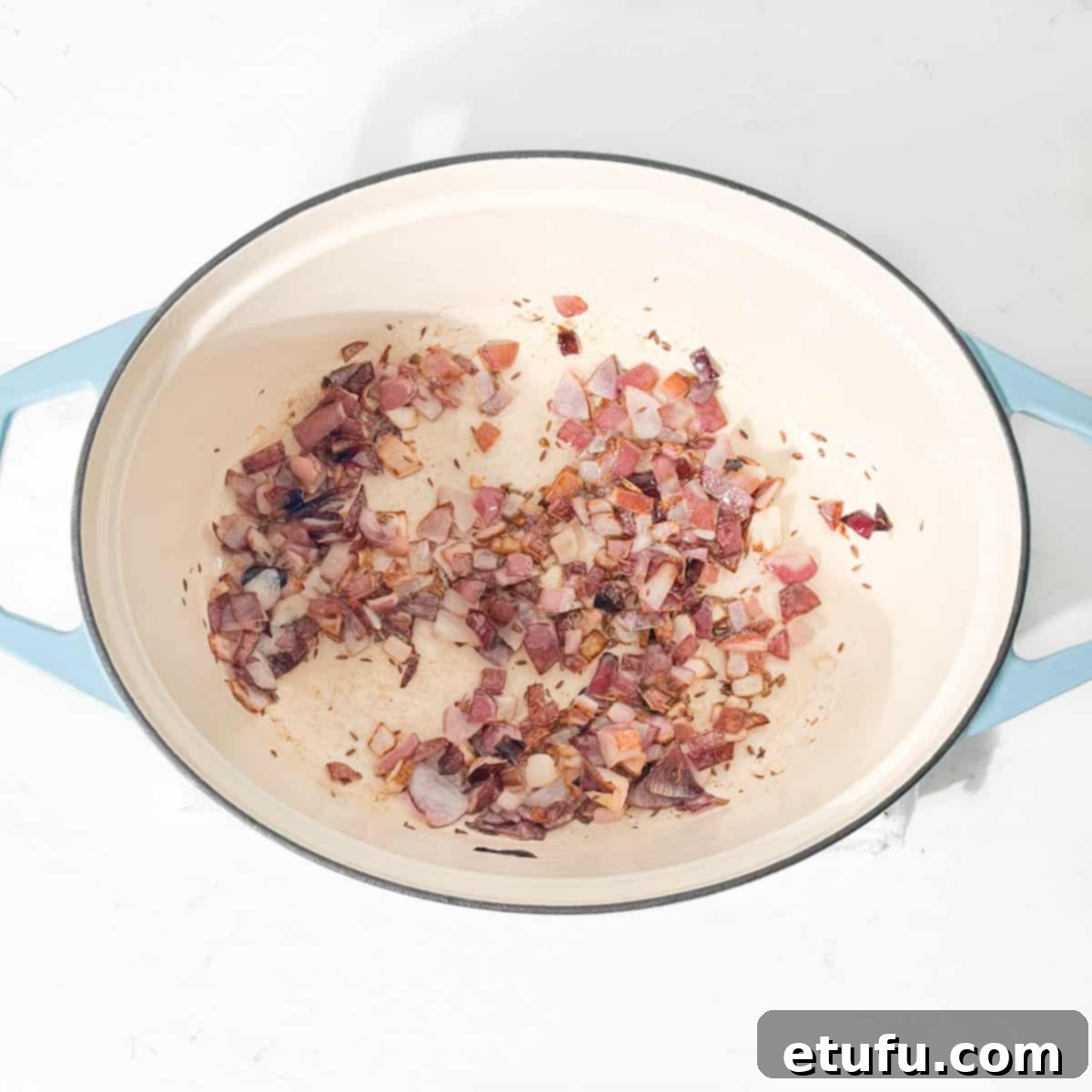 Adding onions to hot oil and cumin seeds in a large oval pot.