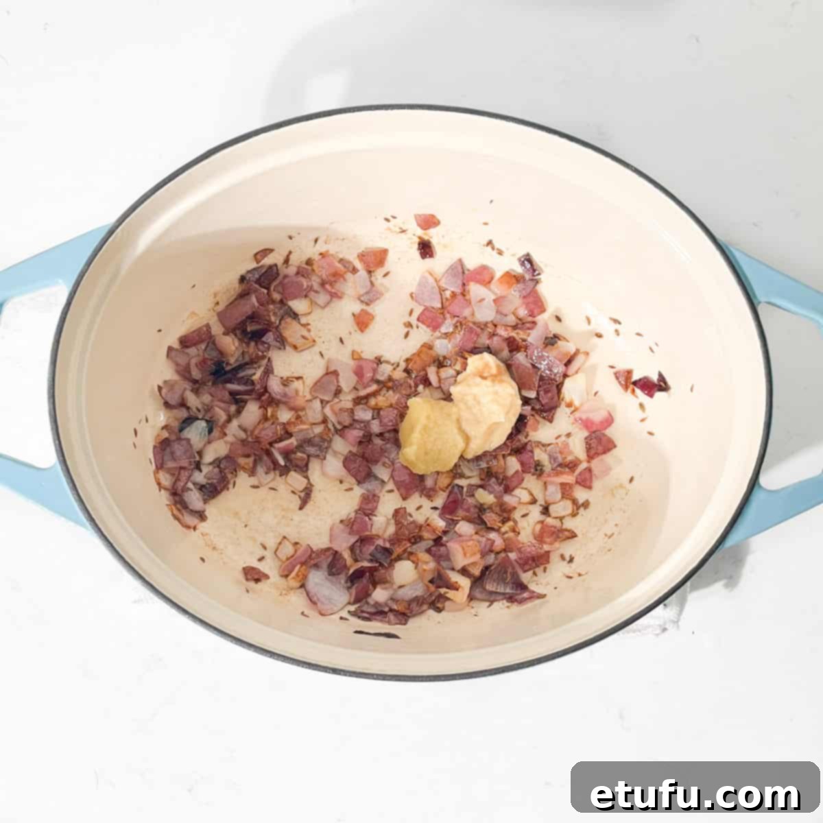 Adding ginger and garlic to the browned onions in a large oval pot.