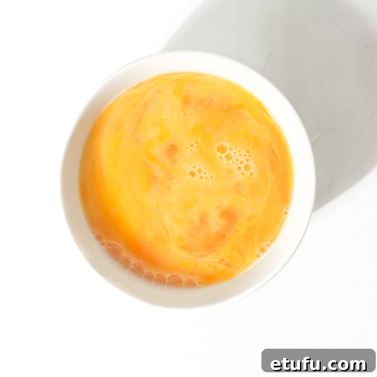 Whisked egg in a small white bowl.