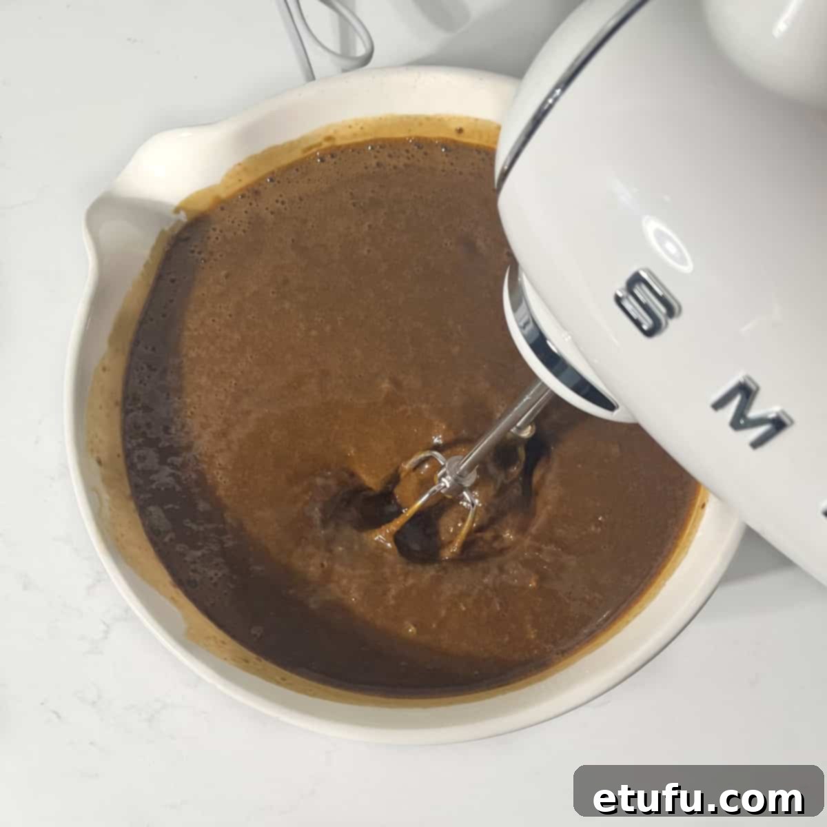 Mixing he batter for Jamaican ginger cake with an electric mixer in a large white mixing bowl.