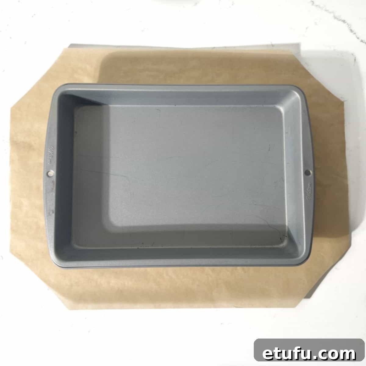 A baking tin on a rectangular piece of baking paper with all four corners cut off.