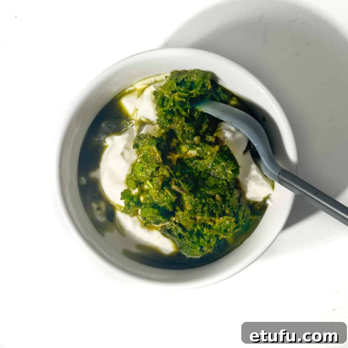 All ingredients are being mixed thoroughly into the yogurt in a small white bowl to form the Indian mint sauce.