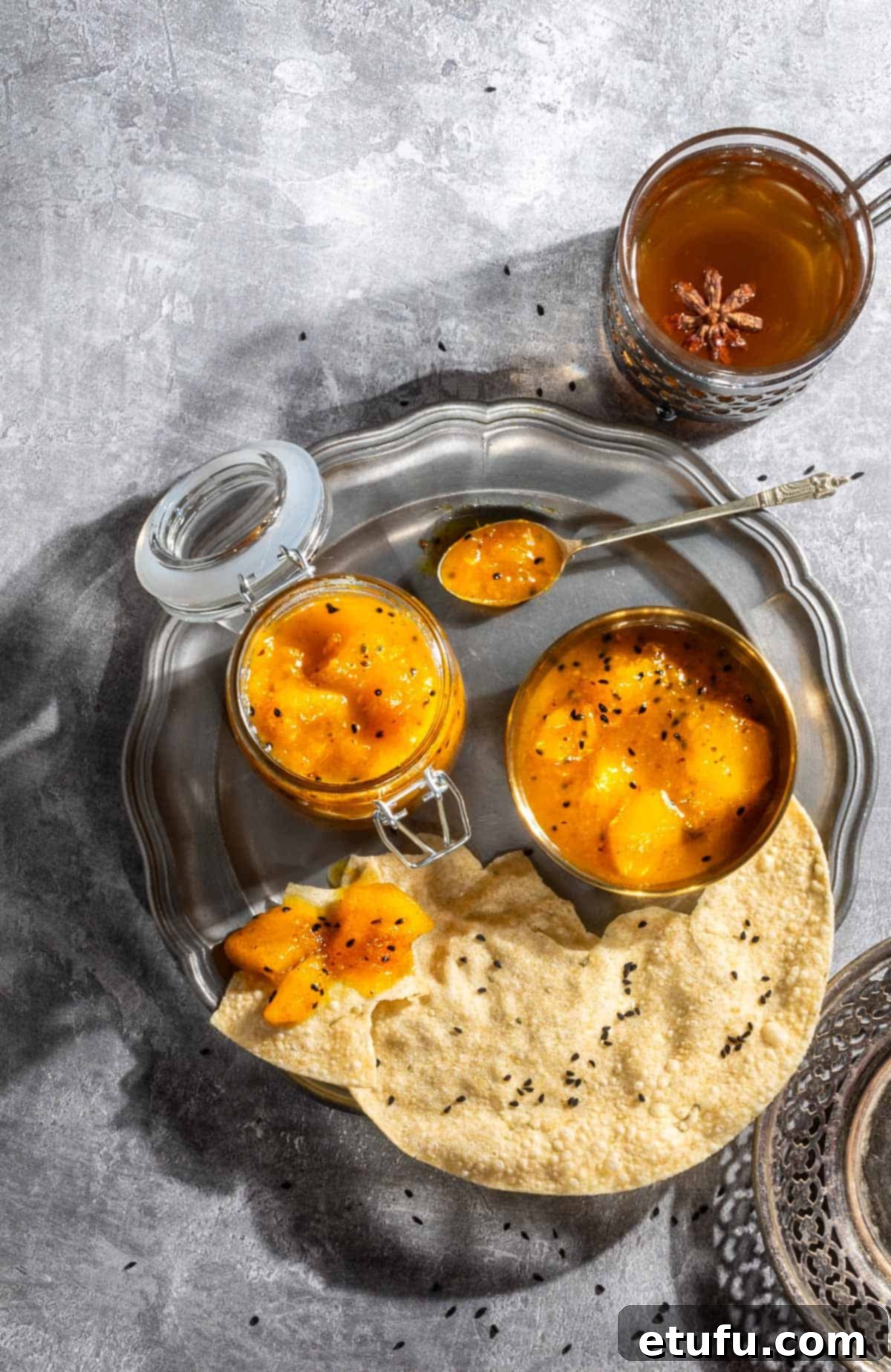 Indian mango chutney in a jar and a bowl with some poppadoms on a plate.