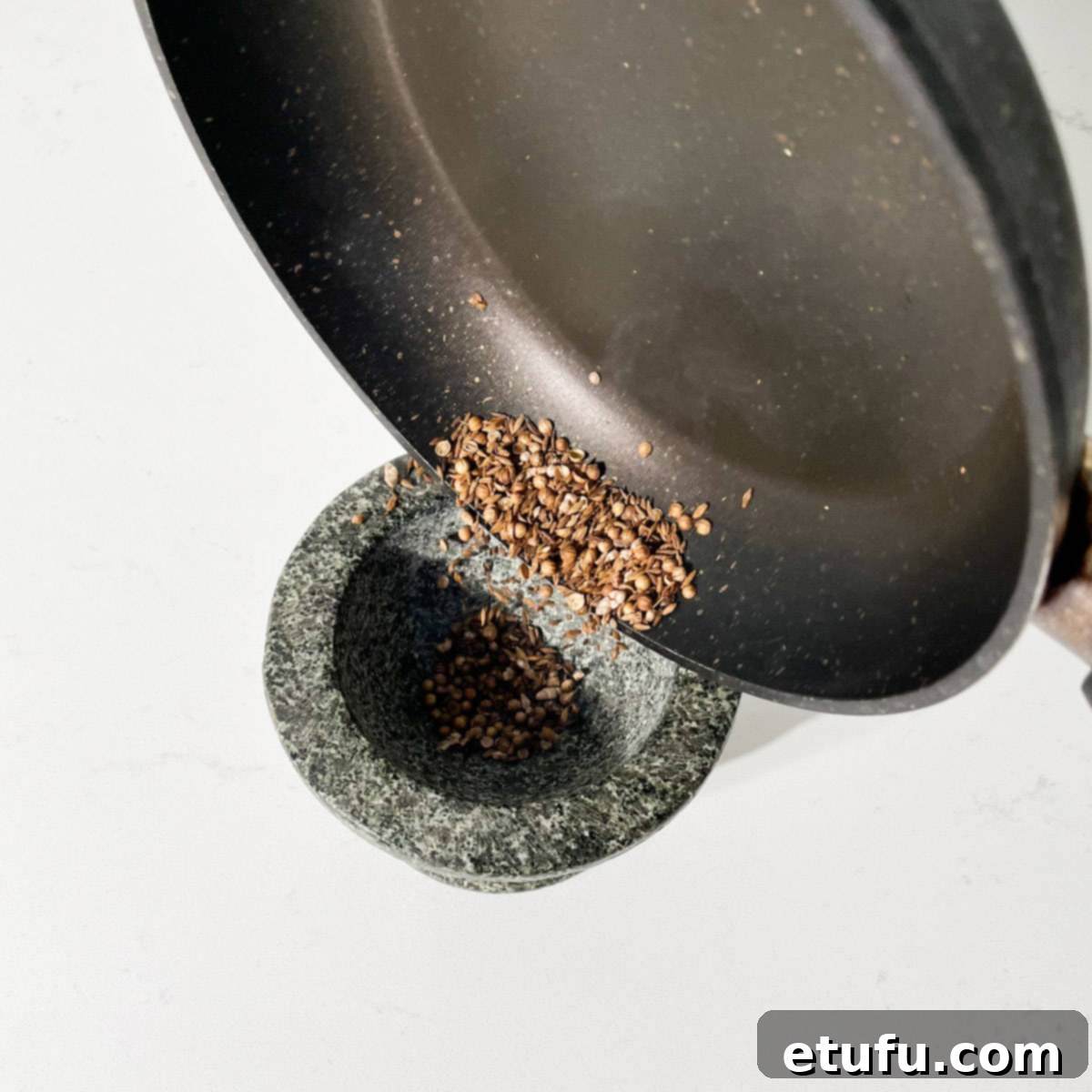 Adding toasted spices to a mortar in pestle.