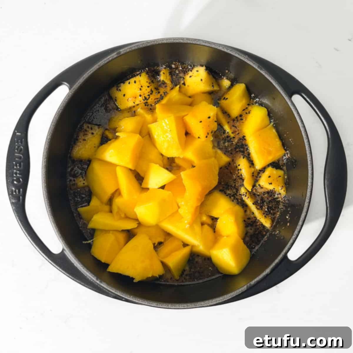 Adding the diced mango to the saucepan along with the rest of the ingredients.