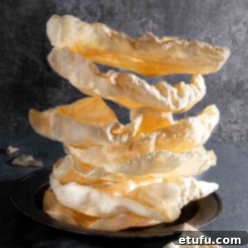 Poppadom Dip Delights 4 A perfectly arranged pile of golden, crispy poppadoms on a white plate against a minimalist grey background.