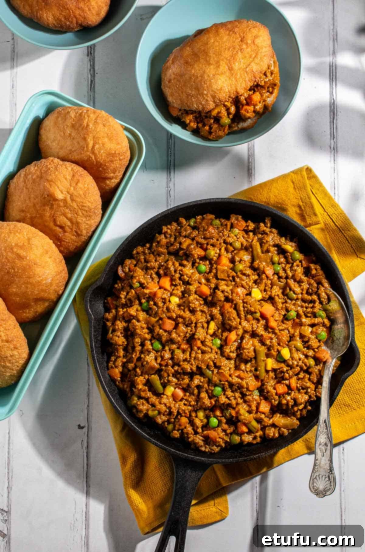 Curried mince in a black cast iron pan with a baking tin full of vetkoek.