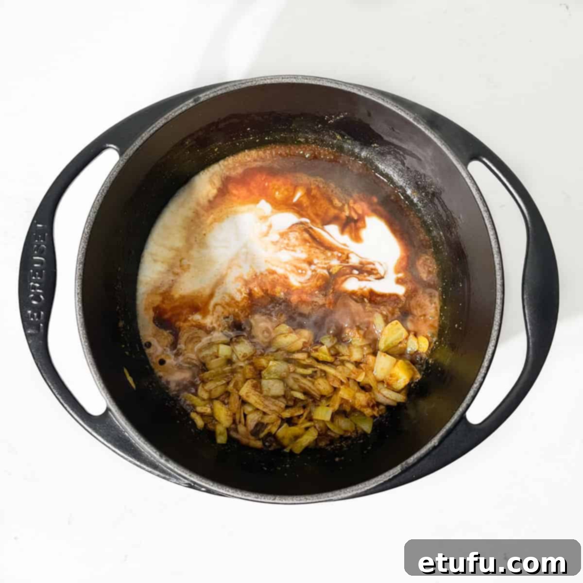 Adding coconut milk and beef stock to the curried onions.