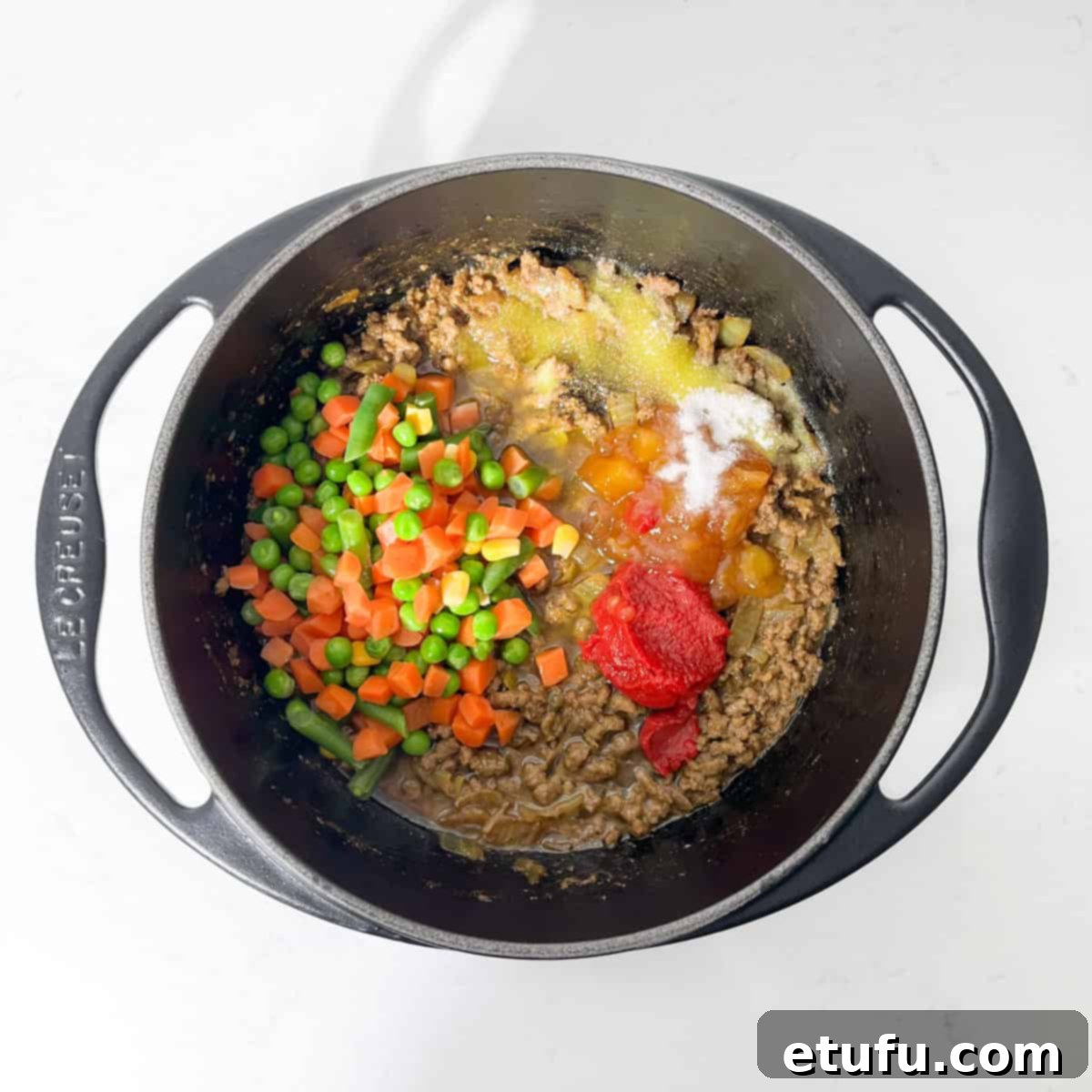 Adding vegetables and other ingredients to the curried mince in a black saucepan.