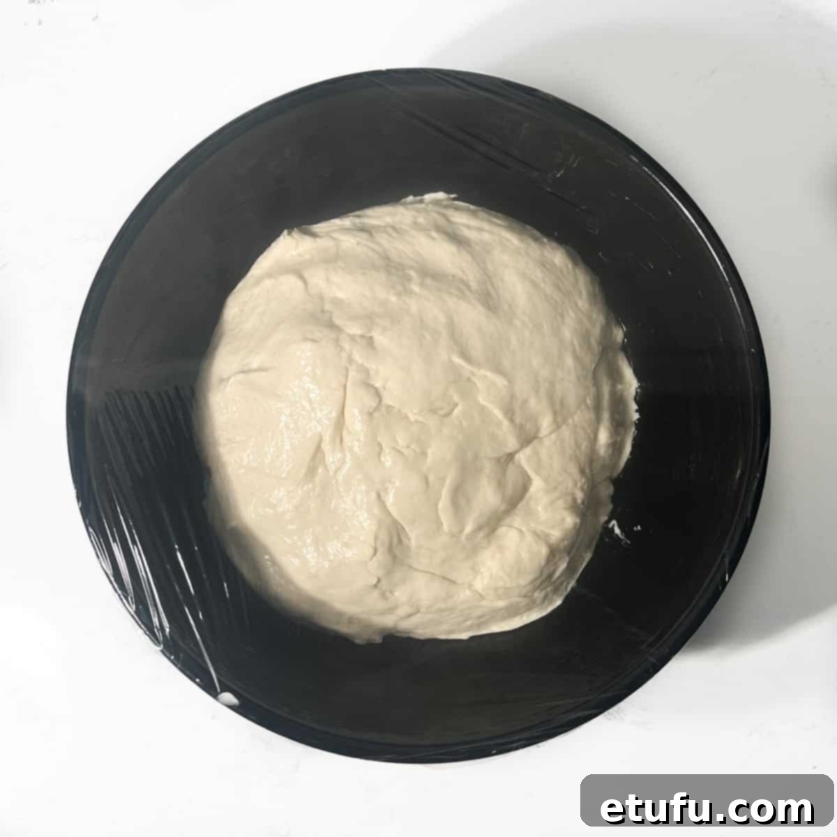 Vetkoek dough in a black bowl, covered with cling film.