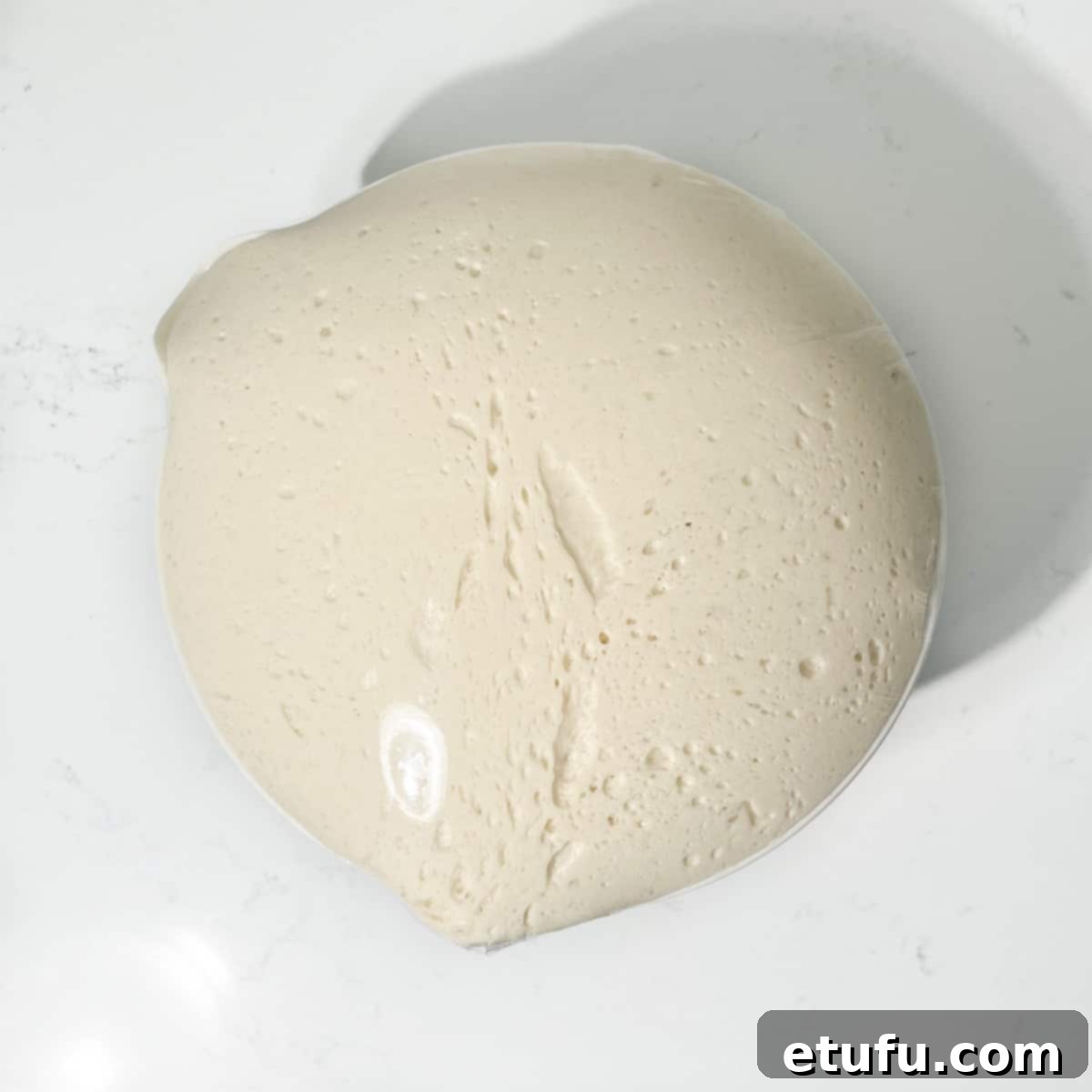 Proofed vetkoek dough in a mixing bowl covered with cling film.