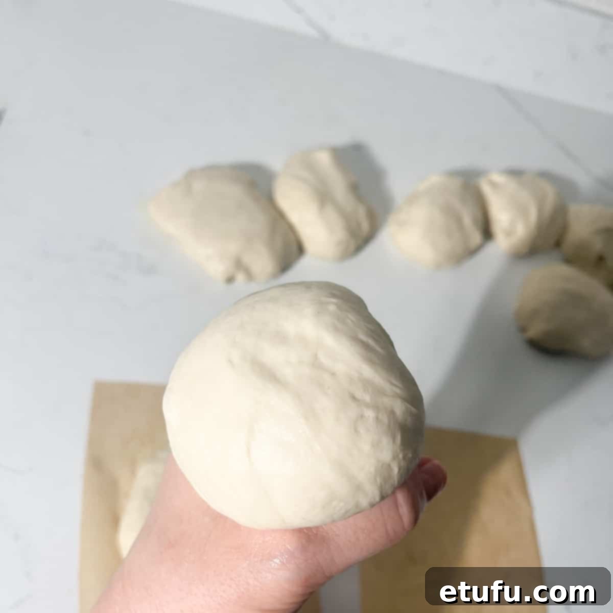 A portion of vetkoek dough being squeezed into a ball between thumb and index finger.