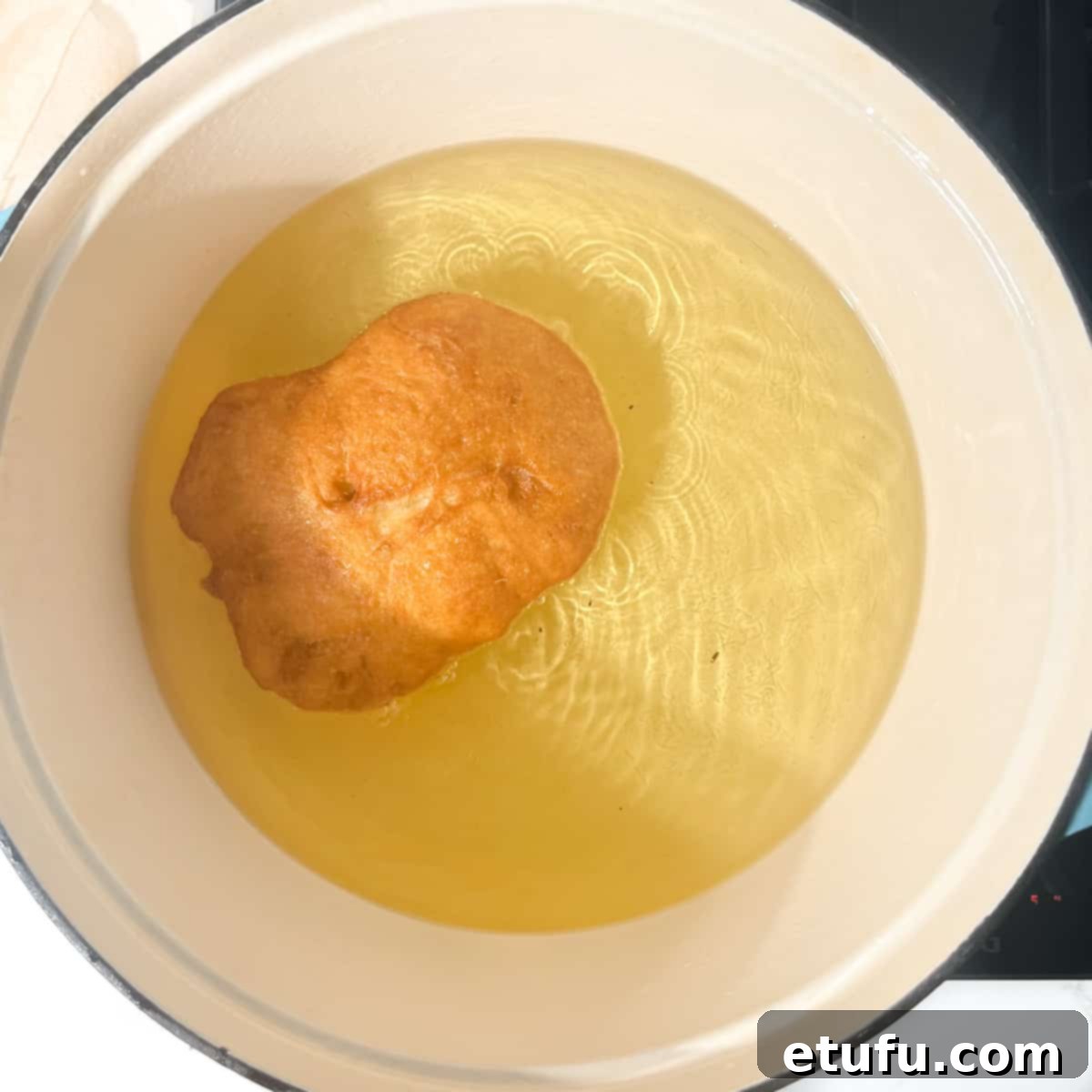 A vetkoek frying in a large saucepan with oil.