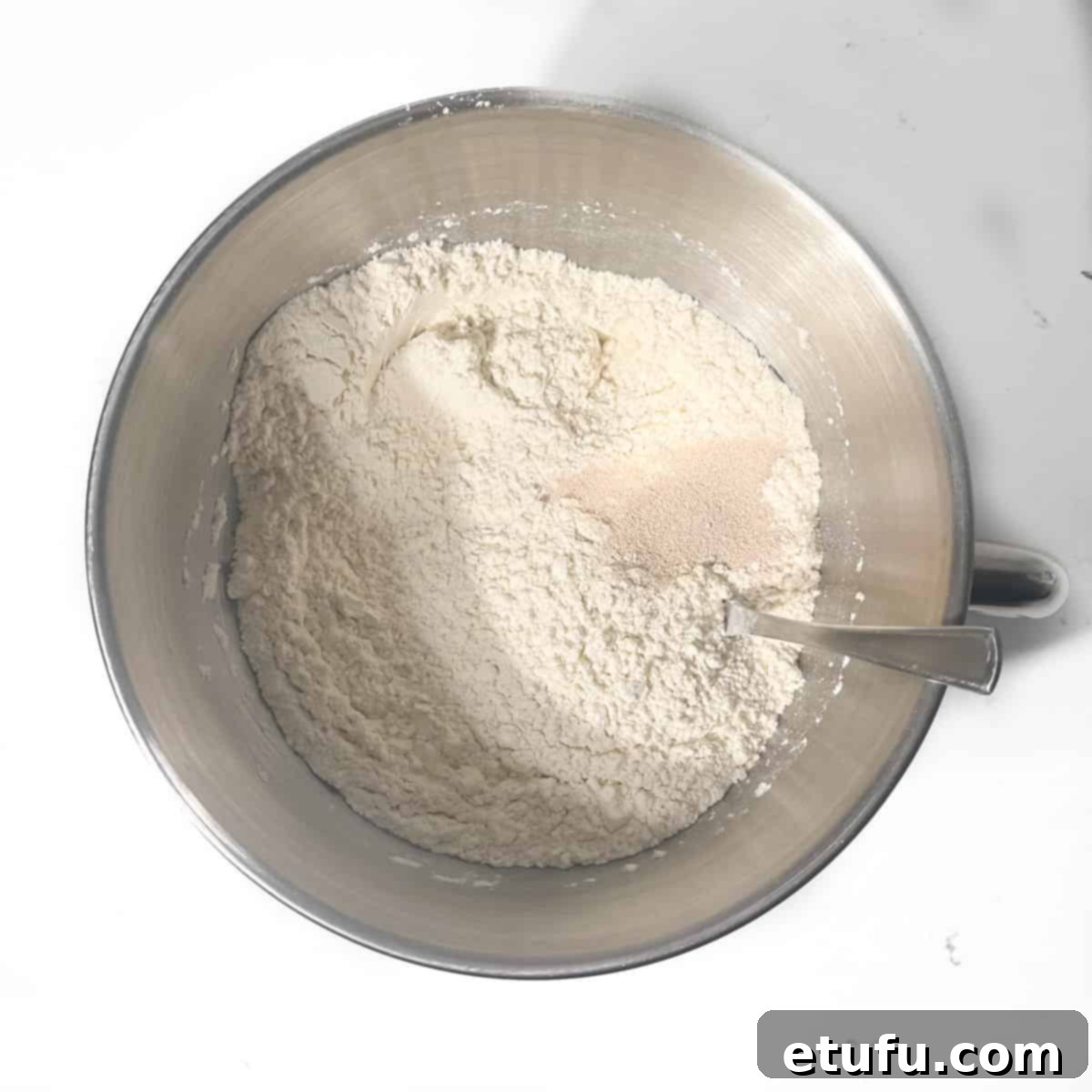 Adding yeast to flour in a large mixing bow.